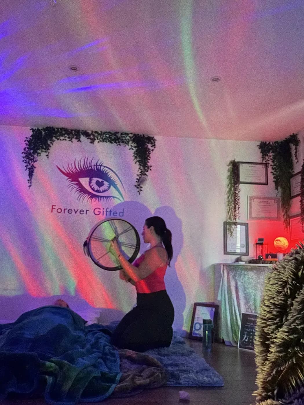 Filiz kneeling with a drum beside a client under aurora light in the cabin