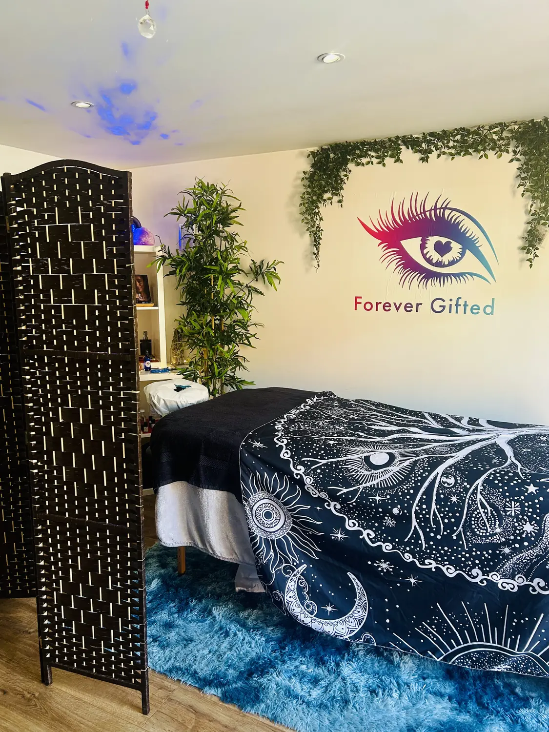 The cabin in daylight with the treatment bed, a starry blanket, plants and the eye on the wall
