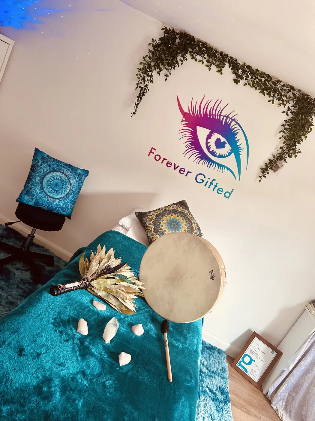 A frame drum, a feather fan and crystals laid out on a teal blanket