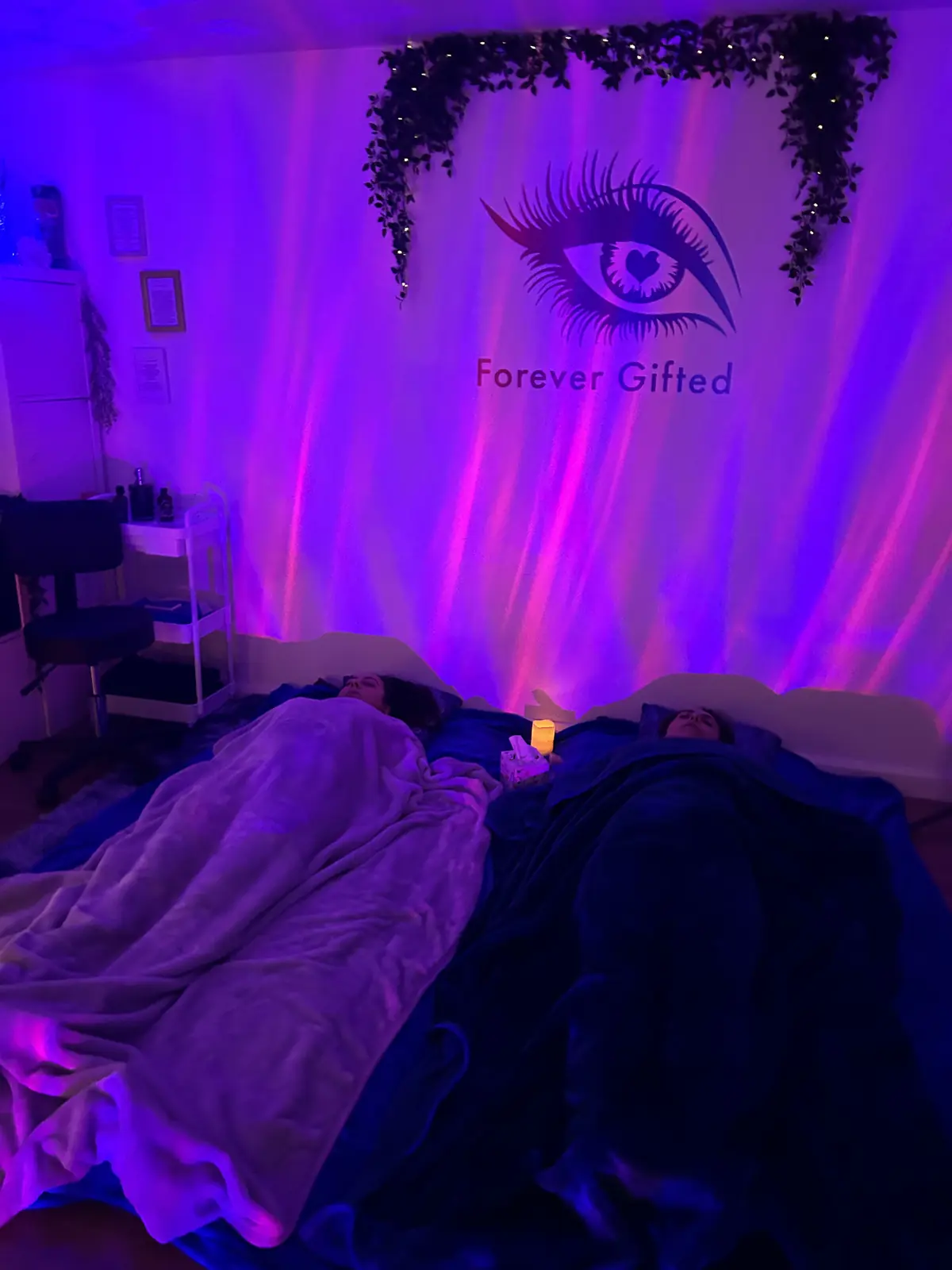 Two people resting under blankets on the cabin floor under aurora light